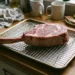 Thick raw tomahawk steak on a wire rack in a sheet pan on a kitchen counter