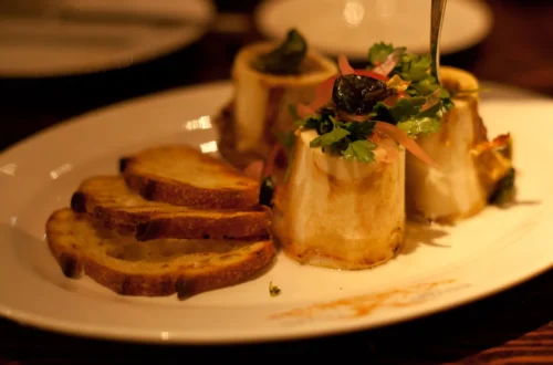 Roasted bone marrow in split beef bones served with toast and parsley salad on a plate