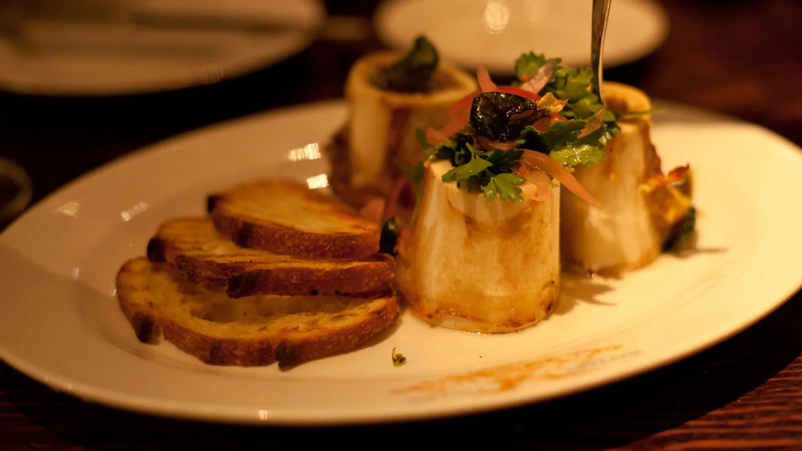 Roasted bone marrow in split beef bones served with toast and parsley salad on a plate