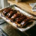 Sheet pan of broiled country style pork ribs with sticky barbecue glaze and charred edges